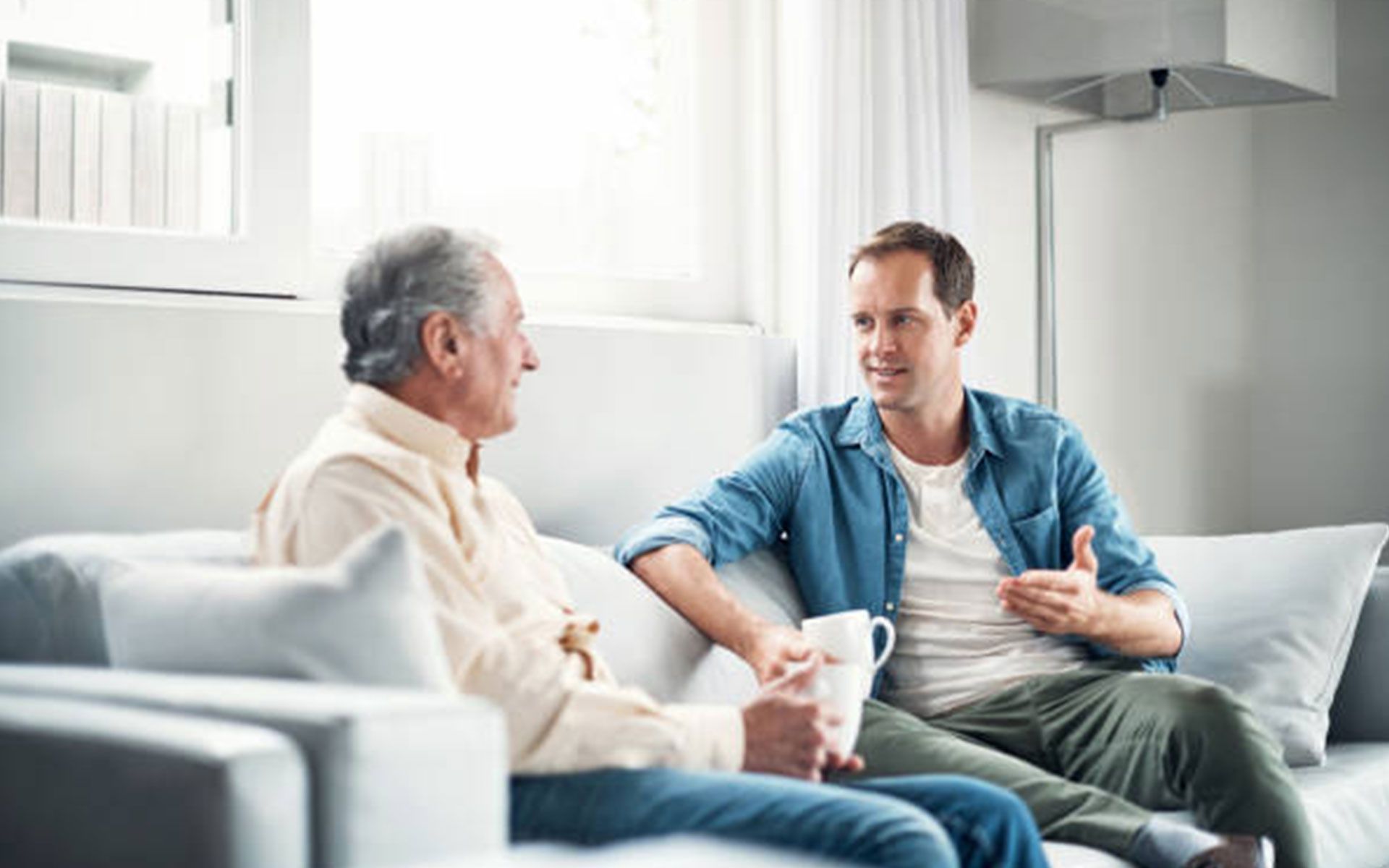 Two men are sitting on a couch talking to each other.