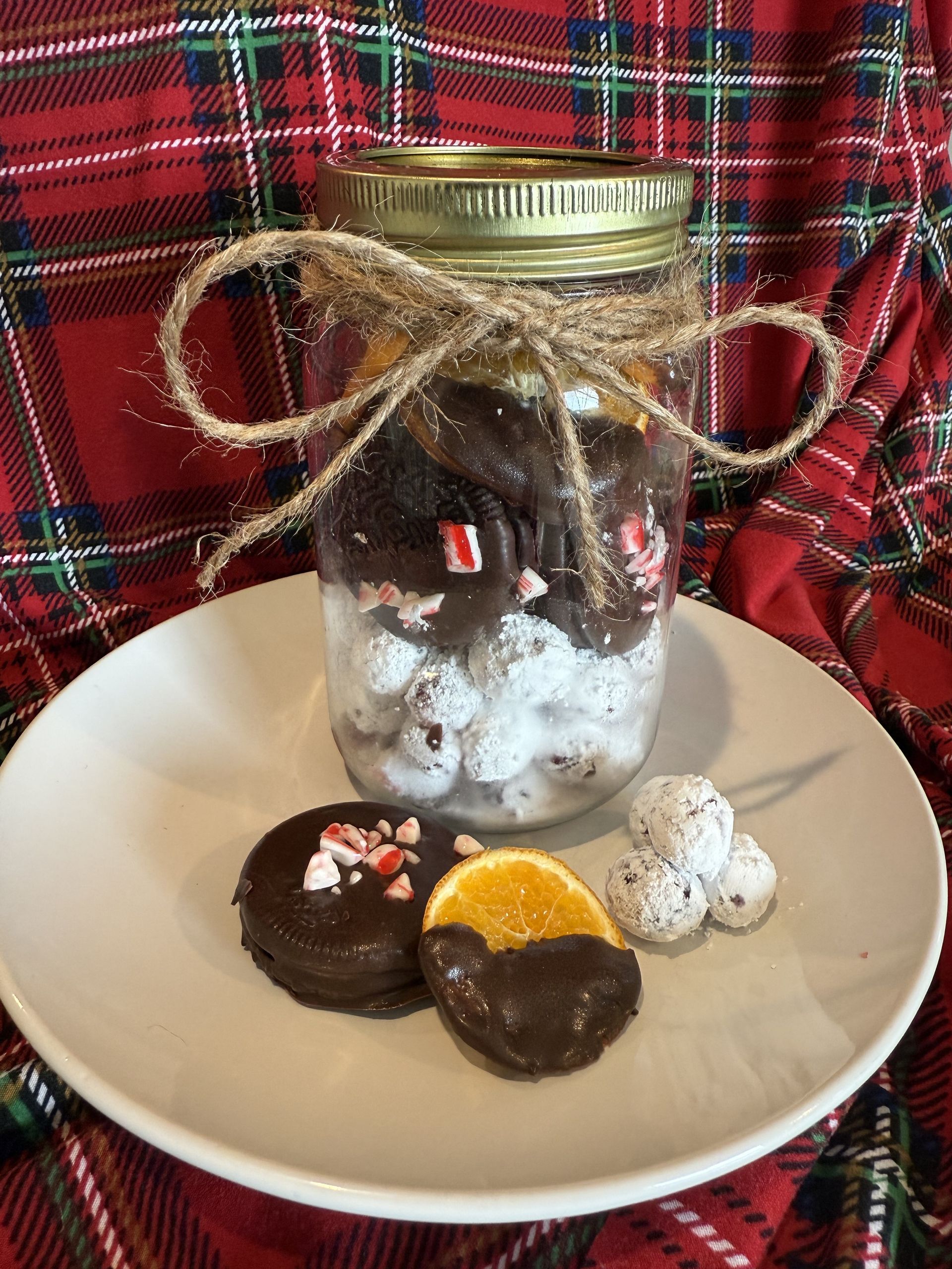 Jar of treats with chocolate-covered peppermint cookie, orange slice, and marshmallow ball on a plate.