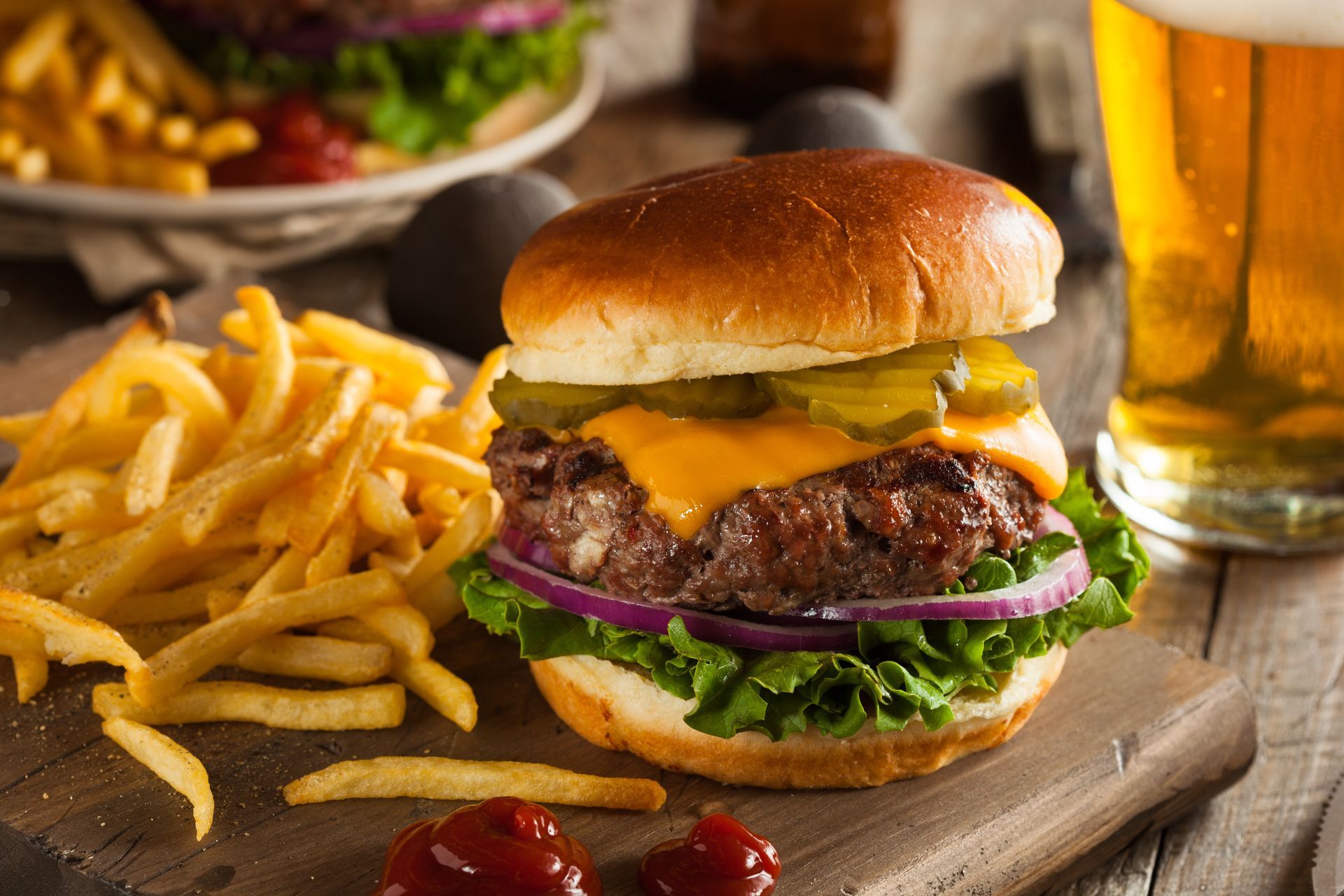Cheeseburger with fries and a beer on a wooden board