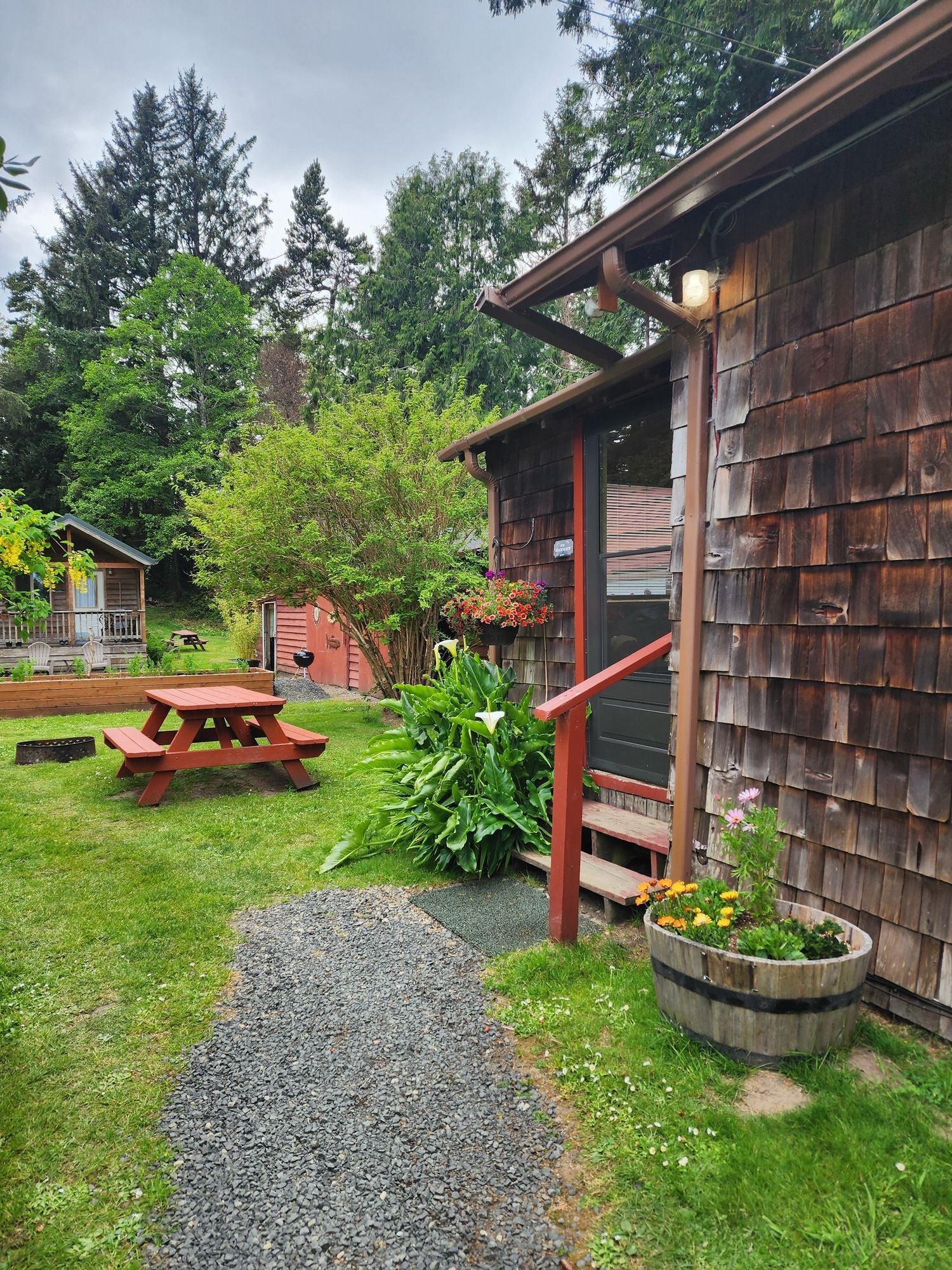Gravel path beside rustic wooden cabin leading to a grassy yard with picnic table and potted plants.