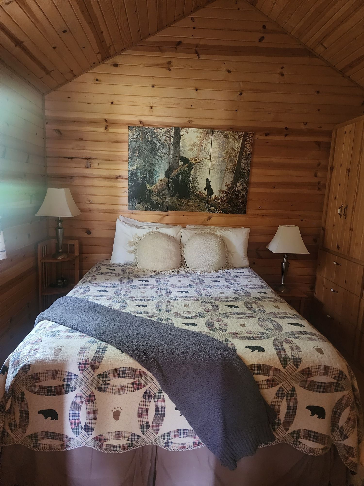 Cozy log cabin bedroom with a bed, two lamps, and a landscape painting above the headboard.