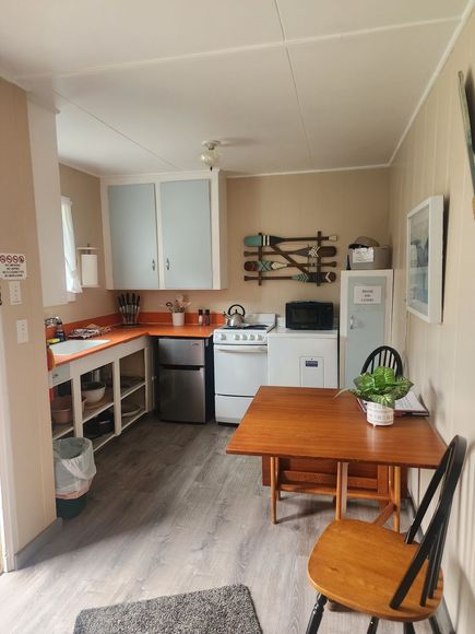 Small kitchen with orange counters, white stove and cabinets, and a wooden dining table by a chair.