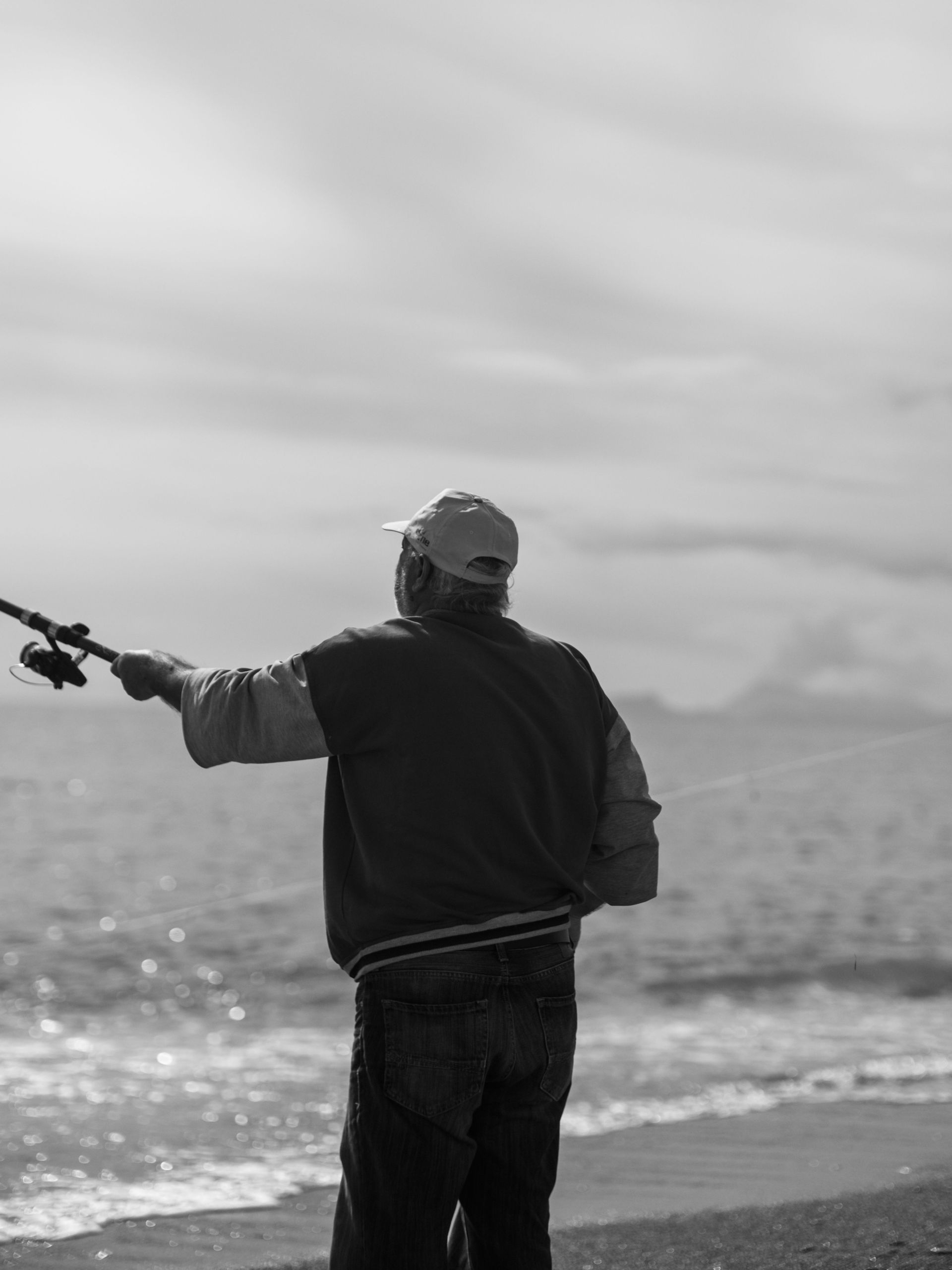 Person fishing from a rocky shoreline under a cloudy sky