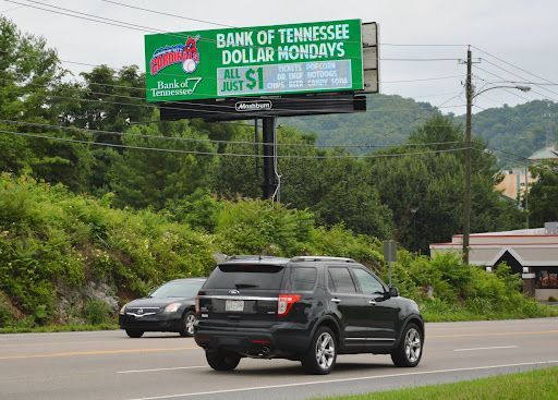 a car is driving down a road in front of a billboard that says bank of tennessee dollar mondays