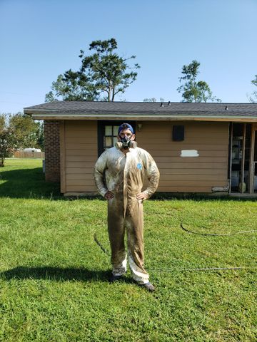 Person in protective suit spraying insecticide near kitchen cabinets.