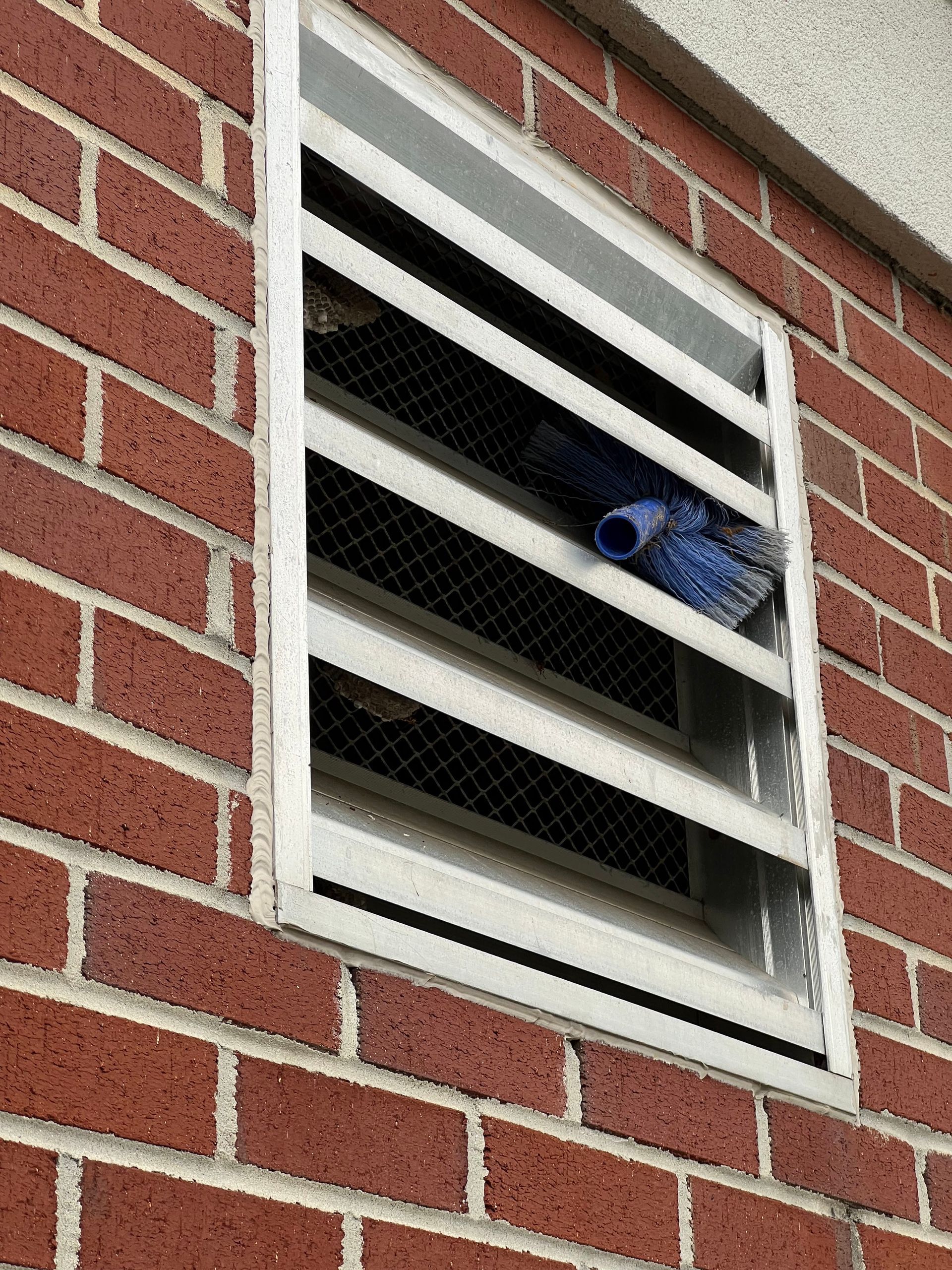 Brick building exterior with a vent window, blue mop inside.