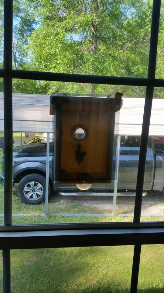 Birdhouse outside a window with a car in the background.