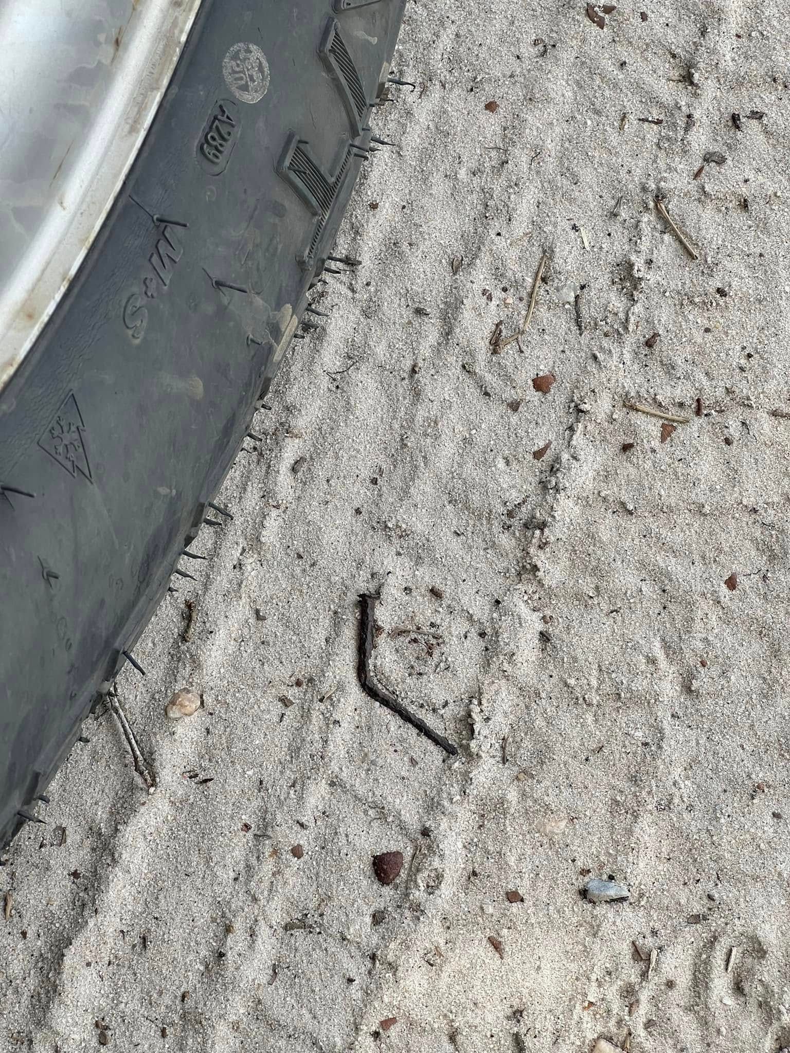 Black metal object near a car tire on sandy ground.