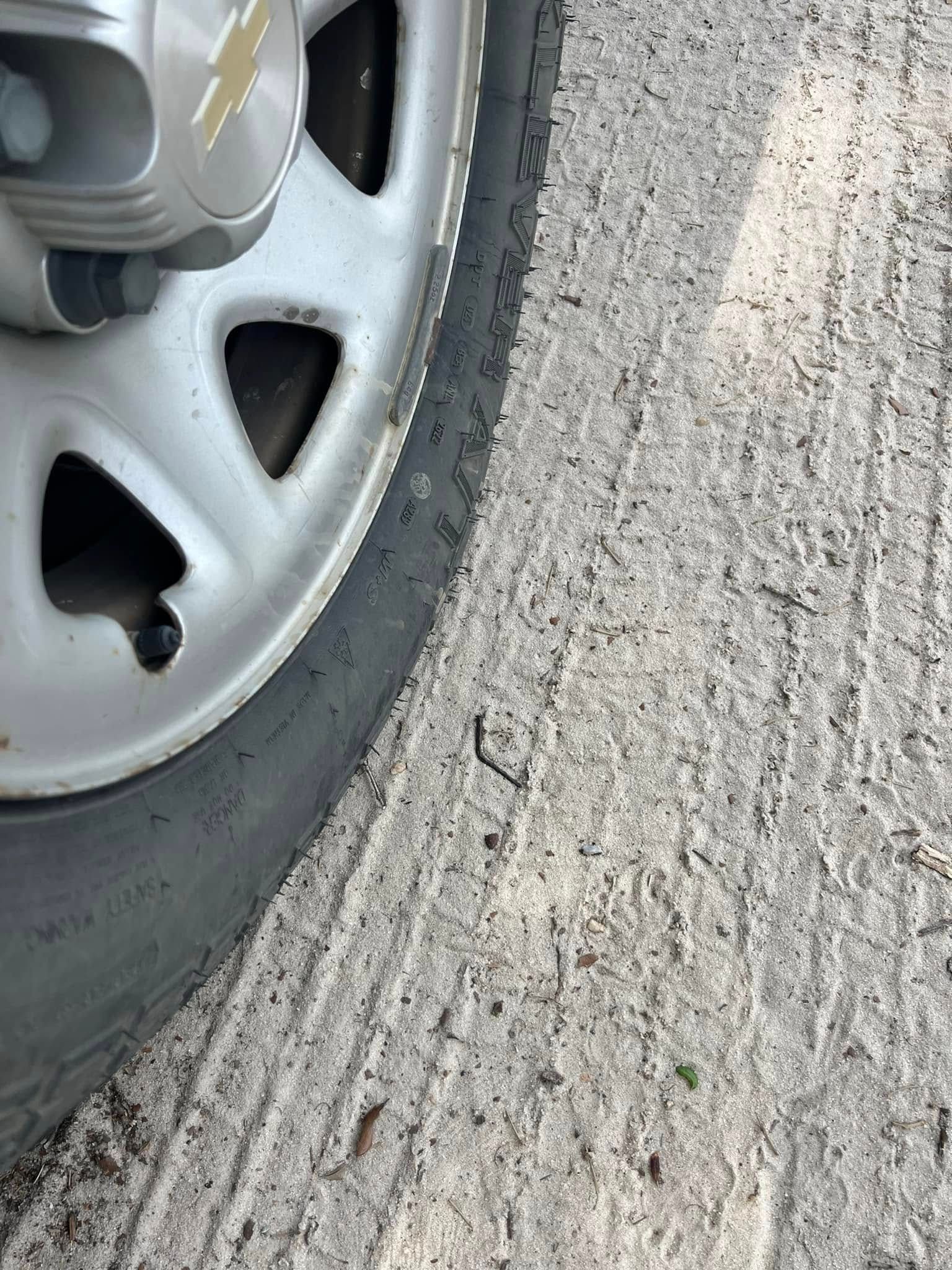 A car wheel, tire, and brake appear on rough, light-colored pavement.