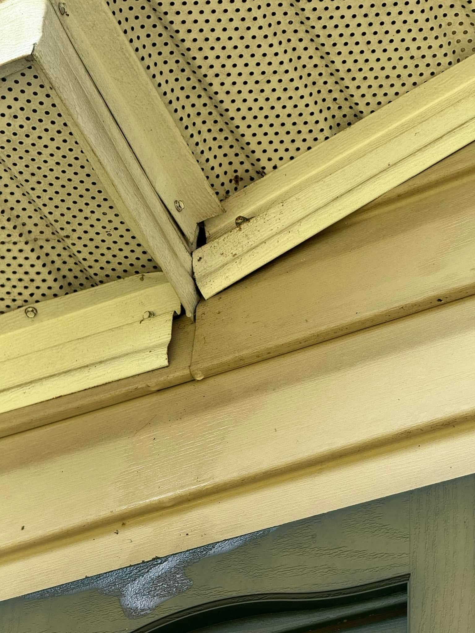 Close-up of a damaged, yellow metal soffit and trim, with visible gaps at the corner joint.