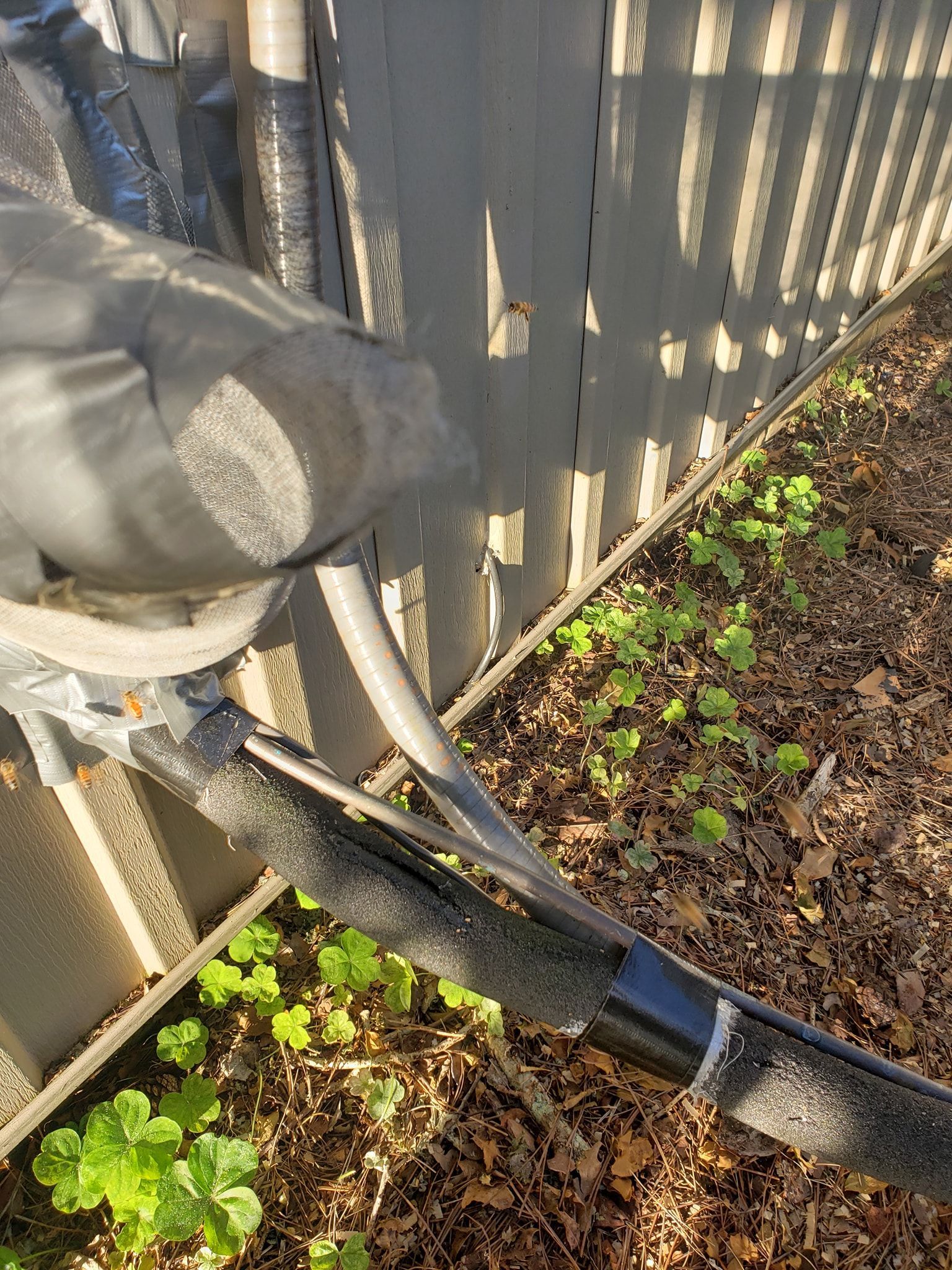 AC unit pipes covered in black insulation near a fence and foliage.