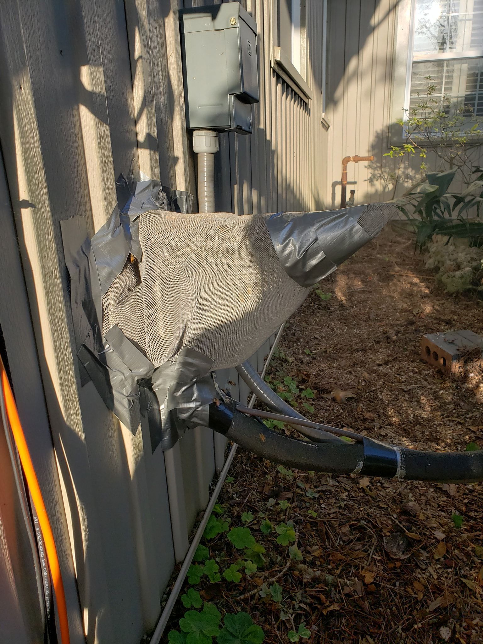 HVAC unit components on exterior wall, heavily taped with duct tape, next to a circuit box.