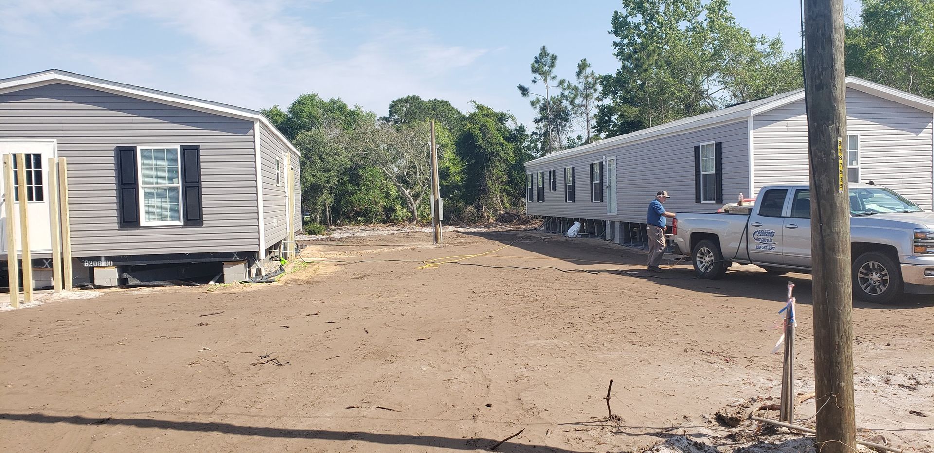 Two mobile homes on a dirt lot, with a truck and person. Blue sky.