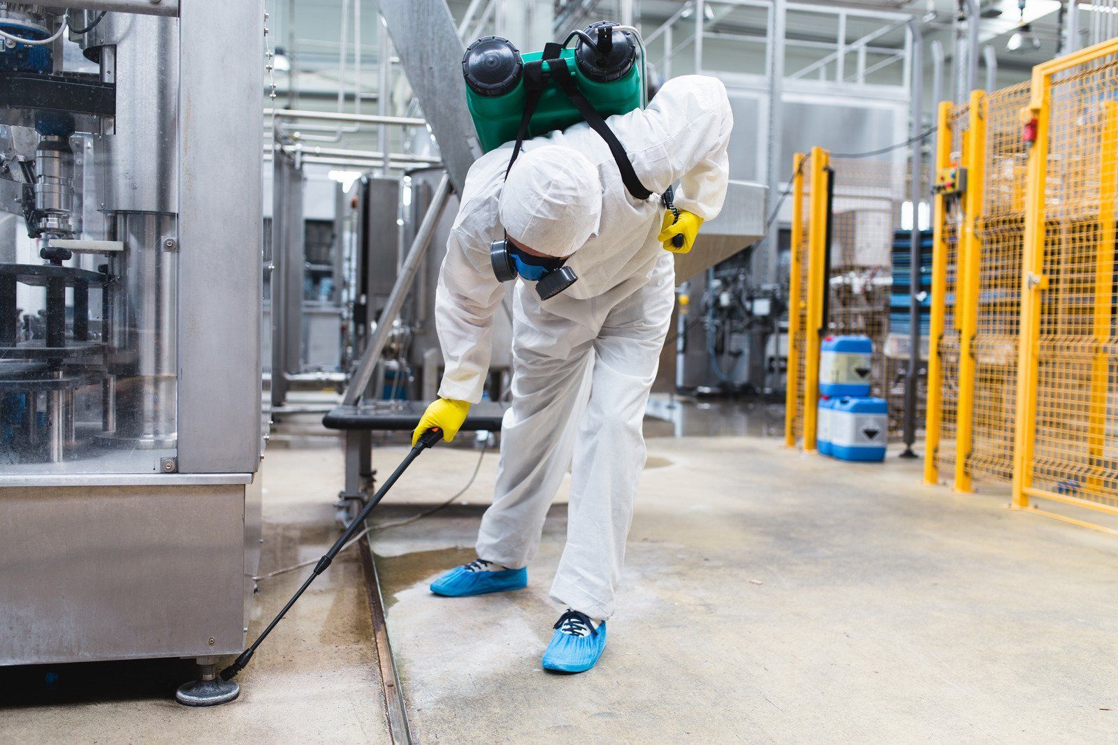 Person in protective suit spraying disinfectant in a factory.