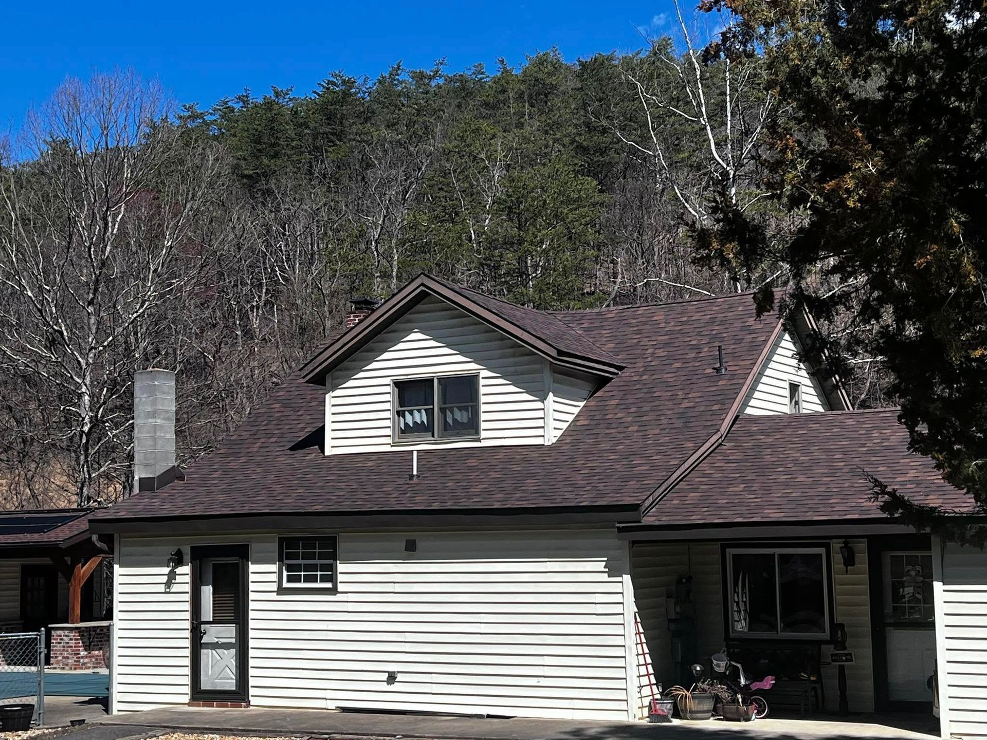 A white house with a brown roof is surrounded by trees.