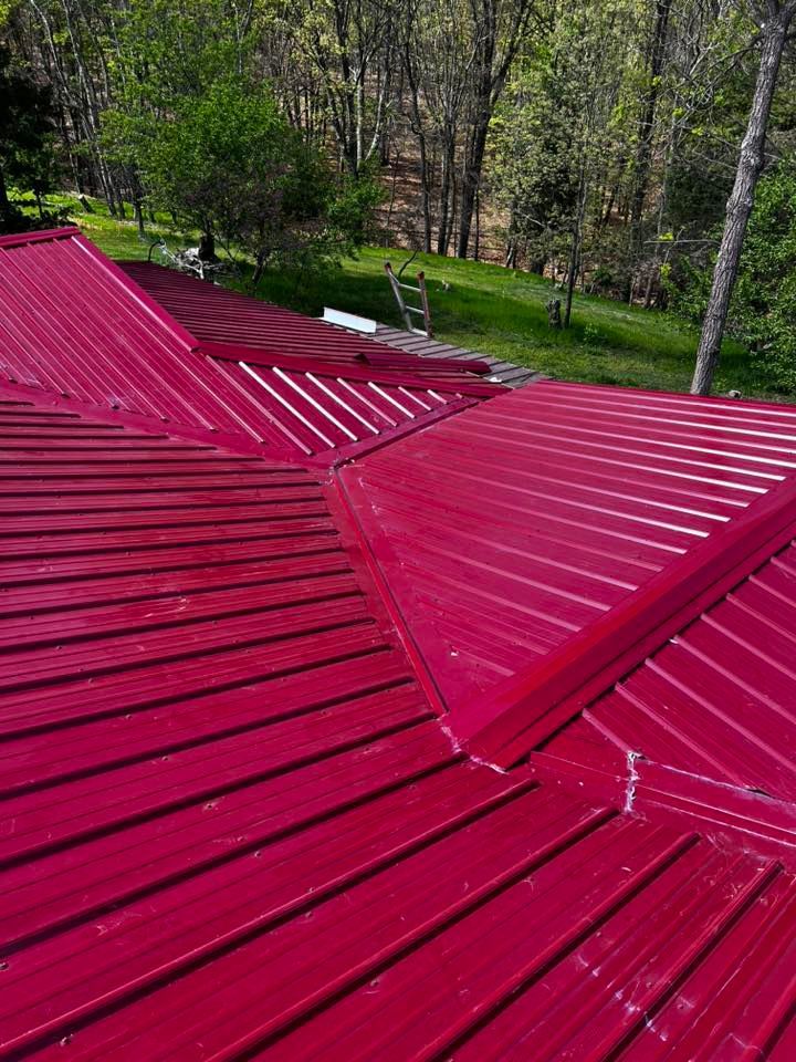 A close up of a red metal roof with trees in the background.