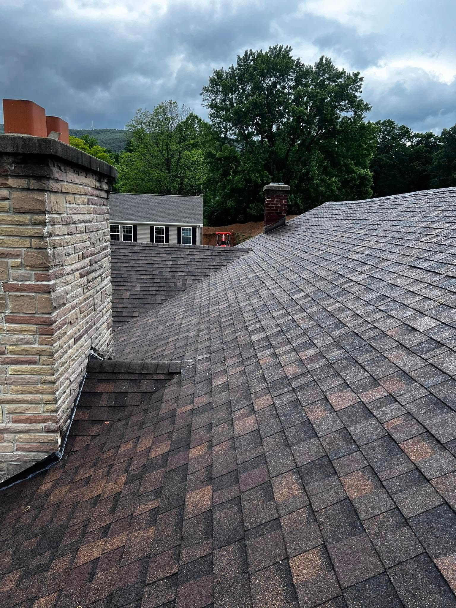 A roof with a chimney and a house in the background.