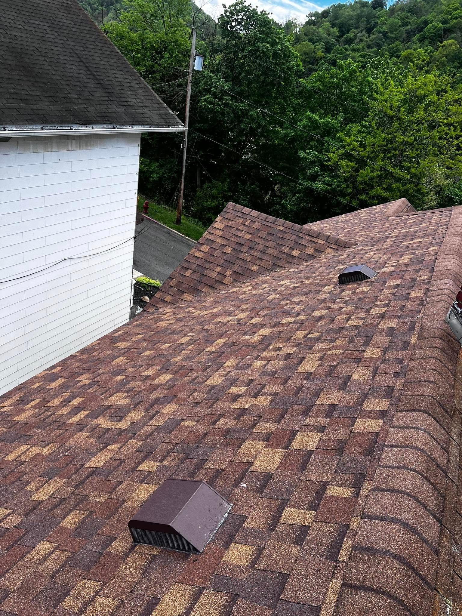 A brown roof with a white building in the background and trees in the background.