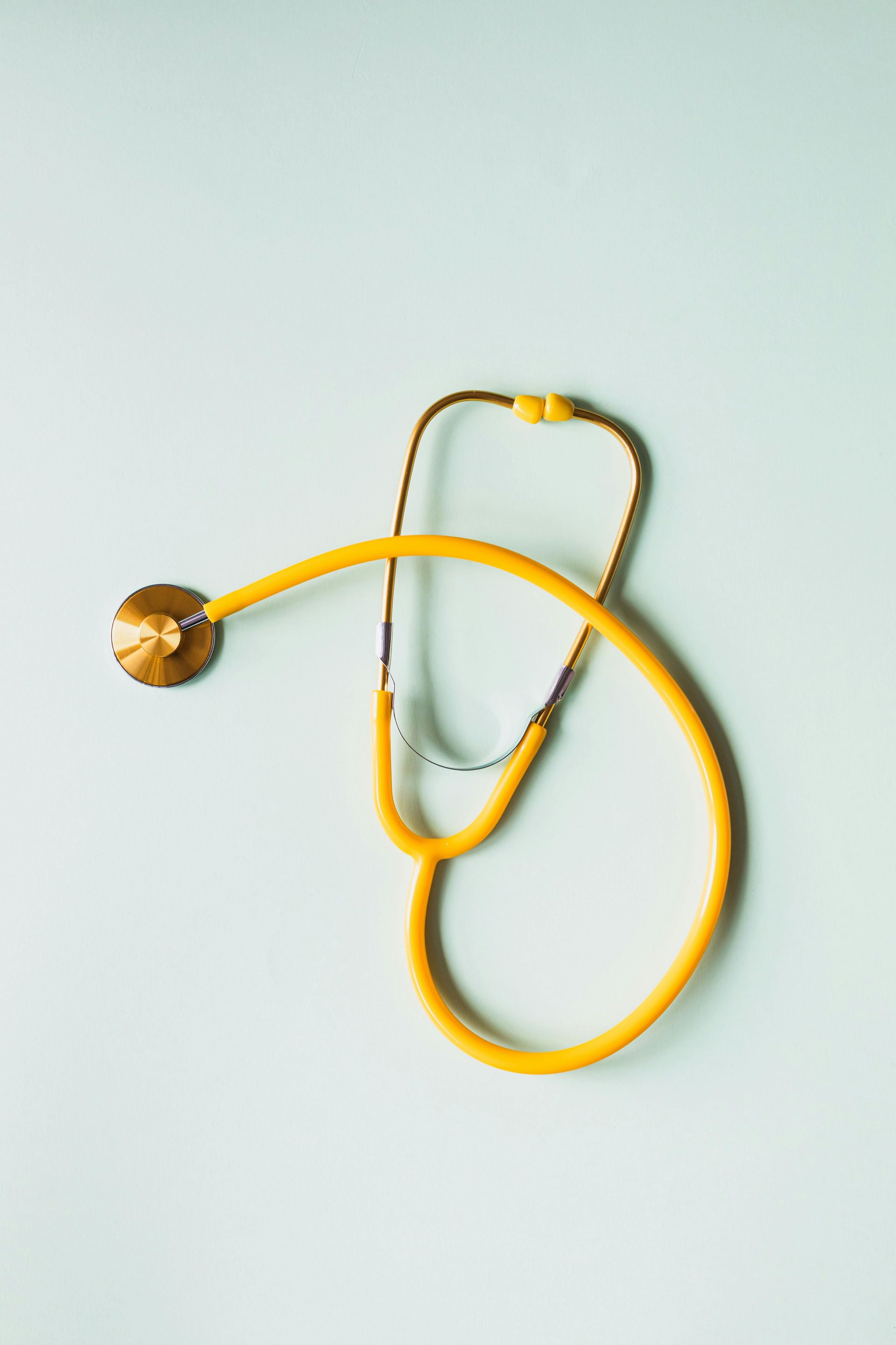 Yellow stethoscope on a light blue background, angled from upper right to lower left.