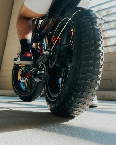 Persoon rijdend op een zwarte elektrische fiets met grote, profielbanden; close-up van het achterwiel.