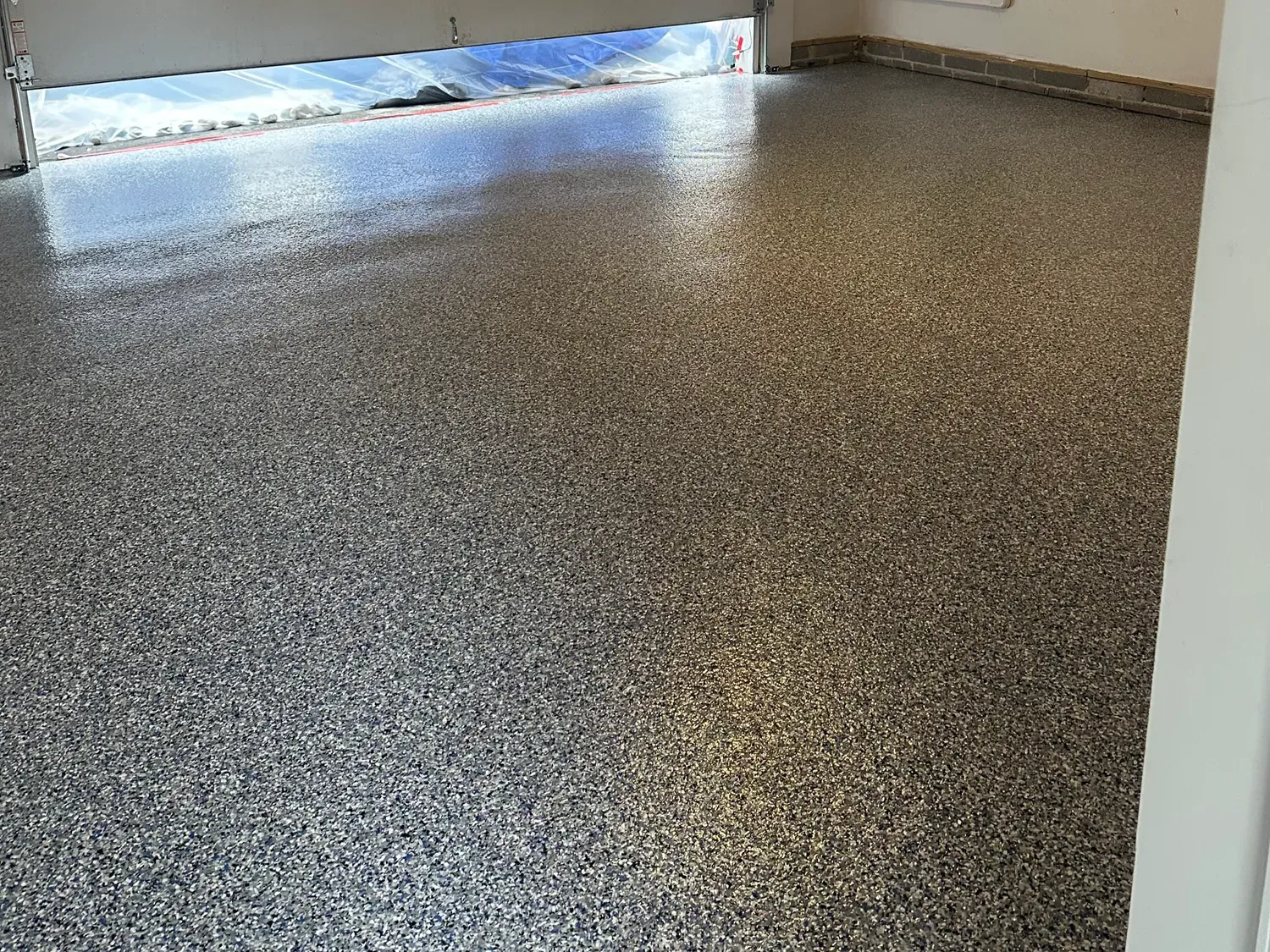Empty room with speckled gray floor and open doorway letting in daylight