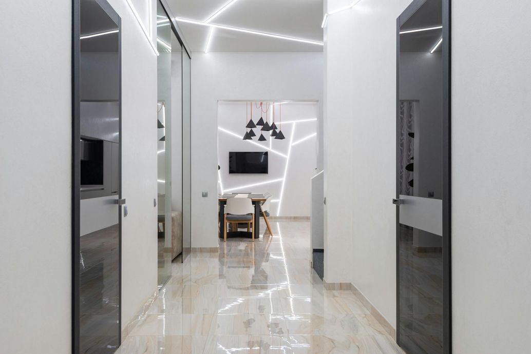 Modern hallway with glossy marble floors, mirrored walls, and a small desk at the end under geometric wall lights