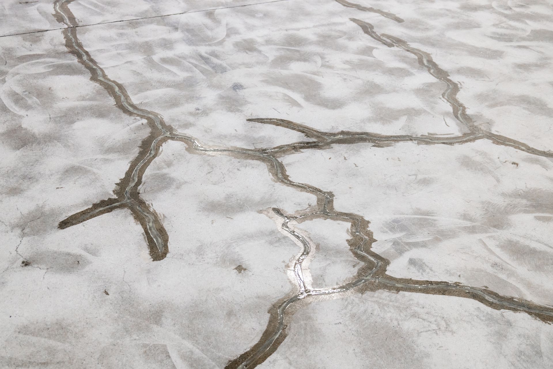 Cracked concrete surface with branching fissures and patchy gray-white stains
