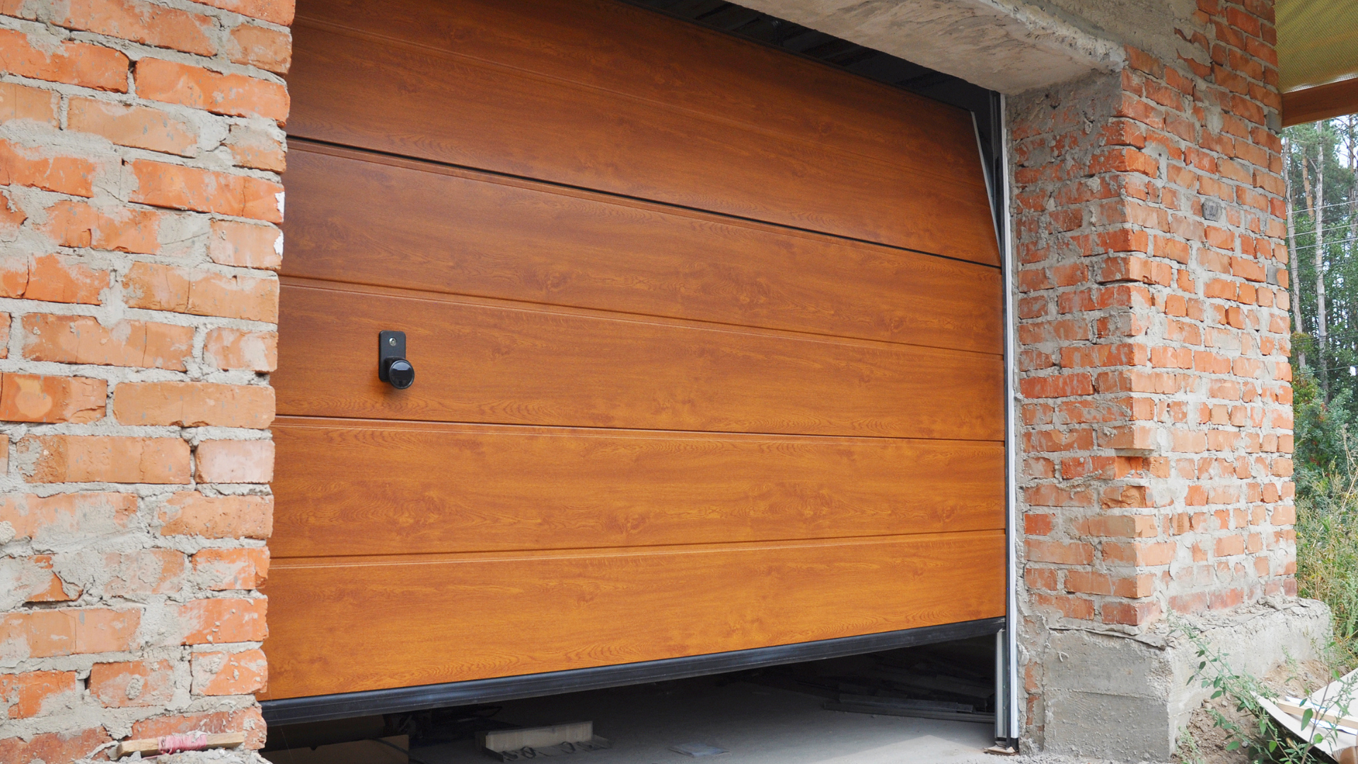 Brown wooden garage door, partially open, set in a brick building under construction.
