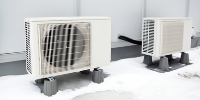 Two outdoor air-conditioning units elevated on blocks in snow