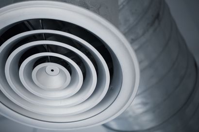 White circular air vent with concentric rings on a gray ceiling