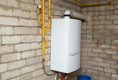 Wall-mounted white boiler with yellow gas pipes in a brick utility room