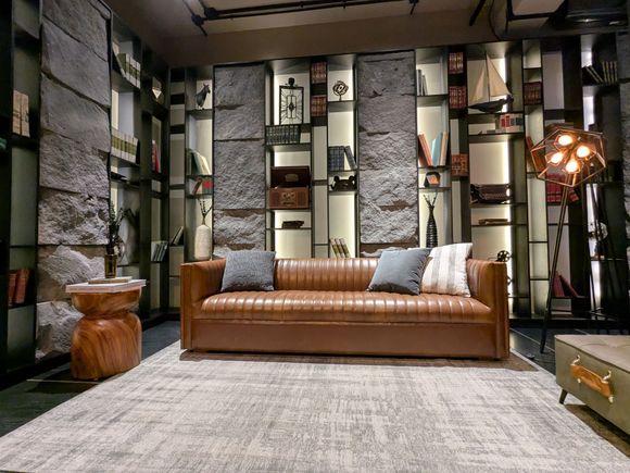 Modern living room with a tan sofa, patterned wall panels, a gray rug, and warm ambient lighting.