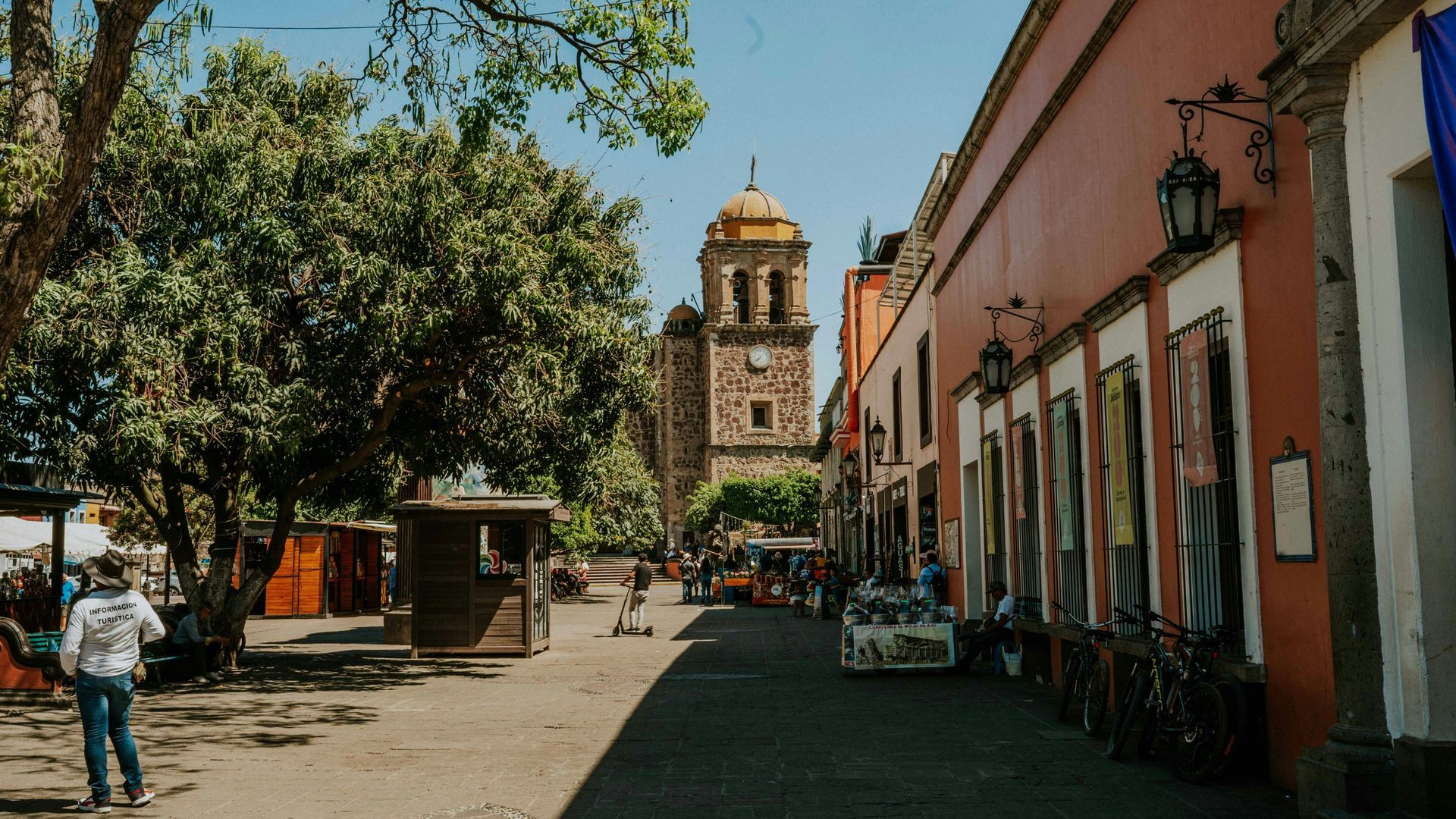 Sunny street with trees, colorful buildings, and a distant church tower.