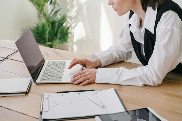 Person typing on a laptop at a desk with papers and a notebook in a bright office.