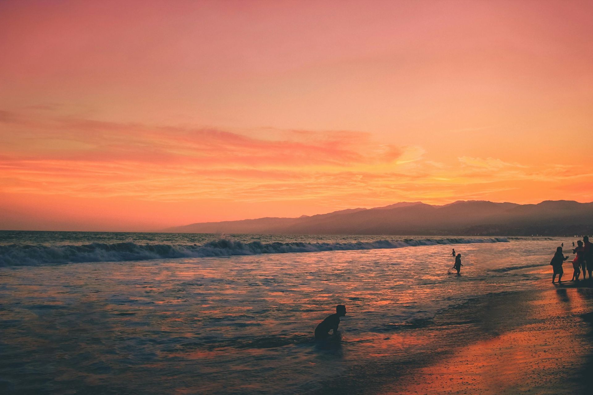 Sunset beach with swimmers in the surf under a pink-orange sky