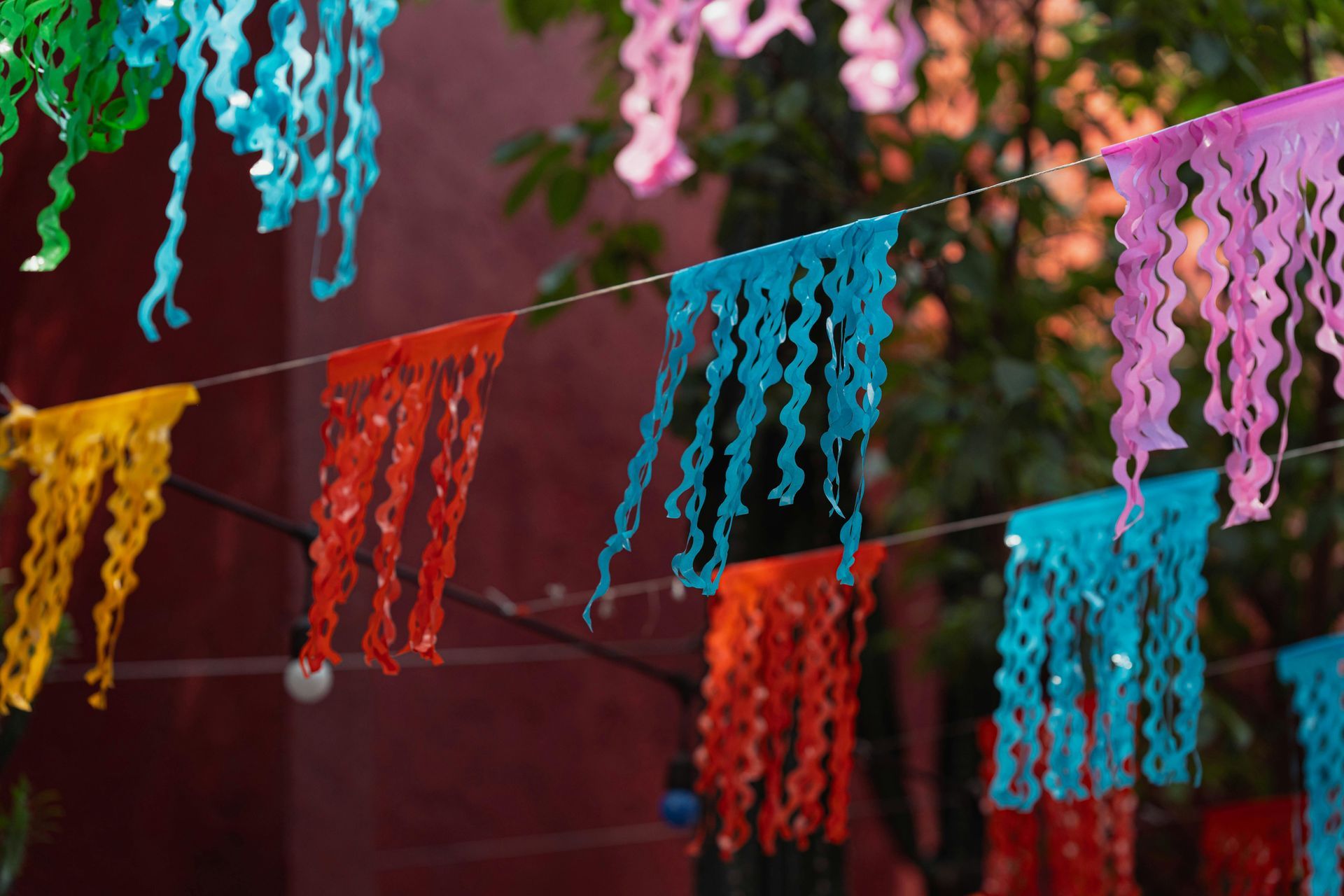 Colorful paper streamers hanging on strings against a blurred red background