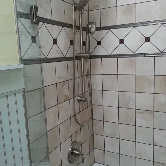 A shower with a tiled wall and a stainless steel shower head