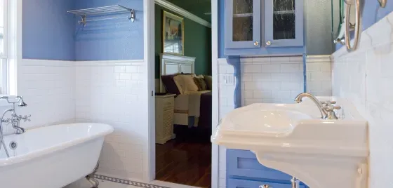 A bathroom with a tub , sink , mirror and blue cabinets.