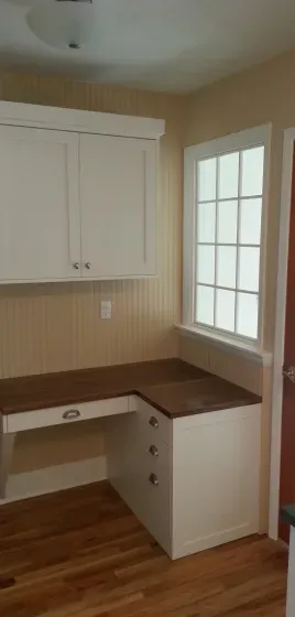 There is a desk in the corner of the room with a window.