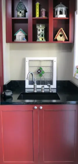 A kitchen with red cabinets , black counter tops , and a sink.
