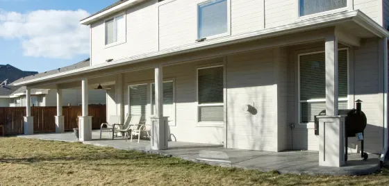 A large white house with a large porch and a grill in the backyard.