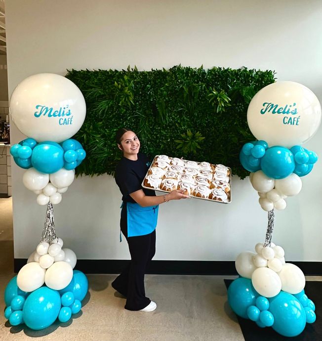 Woman holding cinnamon rolls, flanked by balloon displays with 
