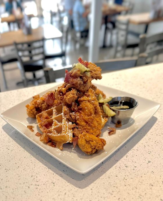 Chicken and waffles with syrup on a white plate in a restaurant.