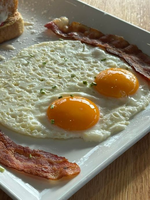 Two sunny-side-up eggs with orange yolks and crispy bacon on a white plate.
