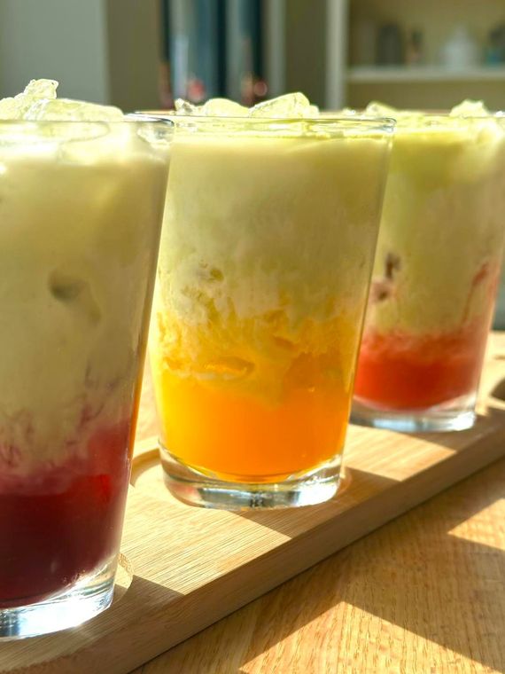 Three layered colorful drinks in glasses on a wooden board; white, orange, and red layers.