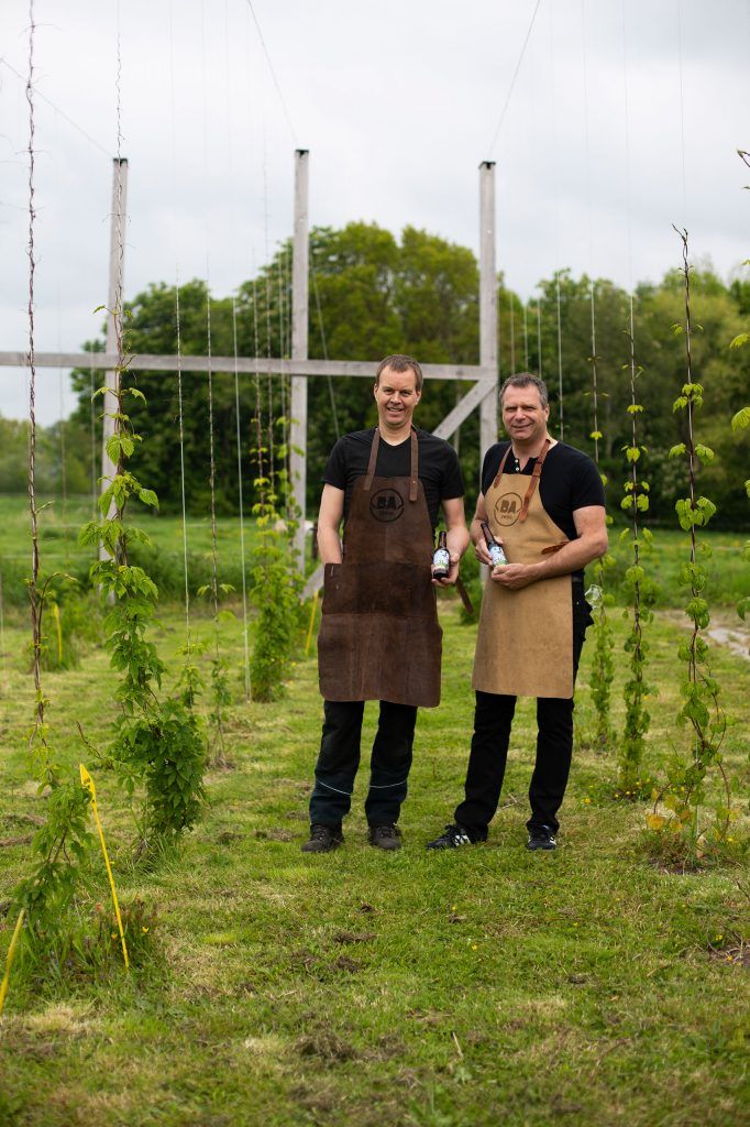 Twee mannen staan in een veld met flessen bier in hun handen.