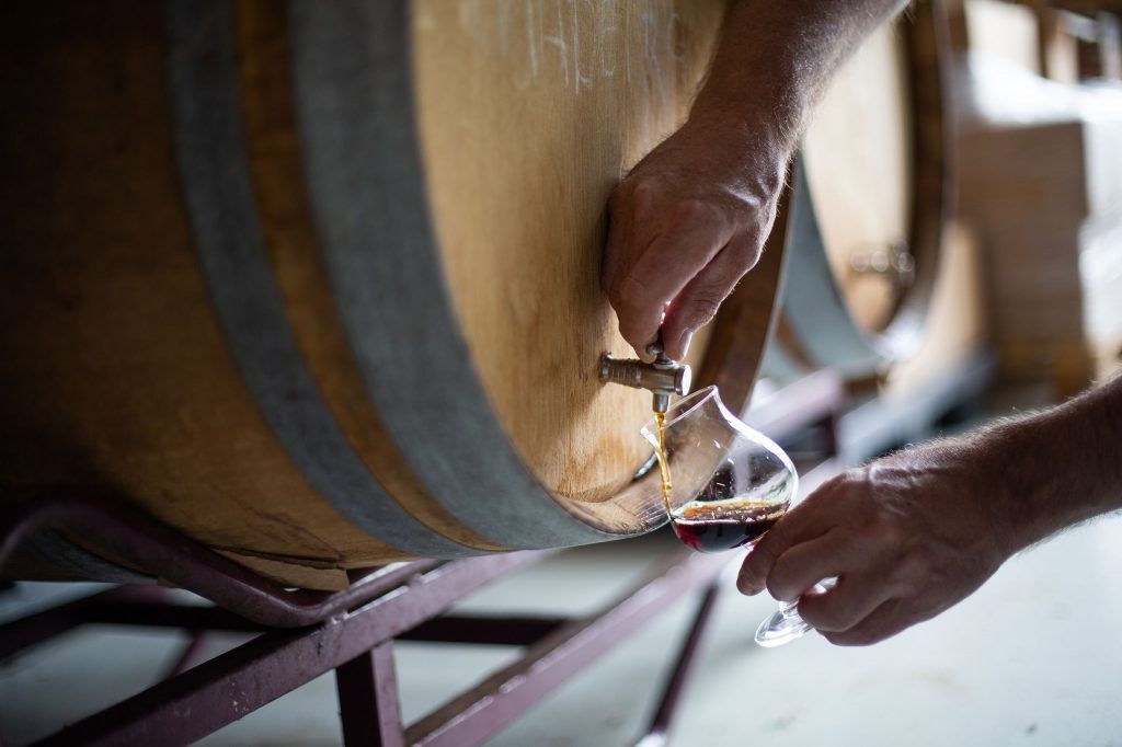 Een persoon giet wijn uit een houten vat in een glas.