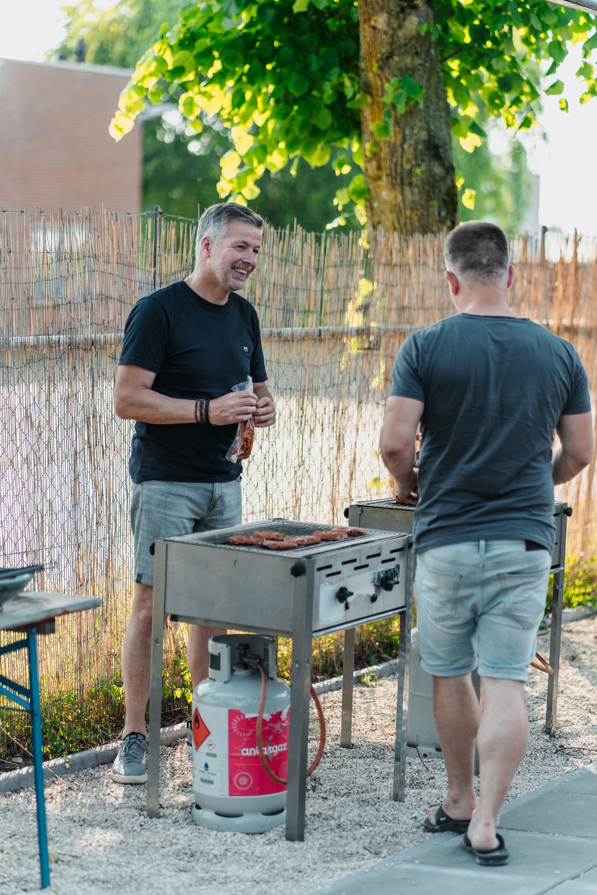 Twee mannen staan naast een barbecue.