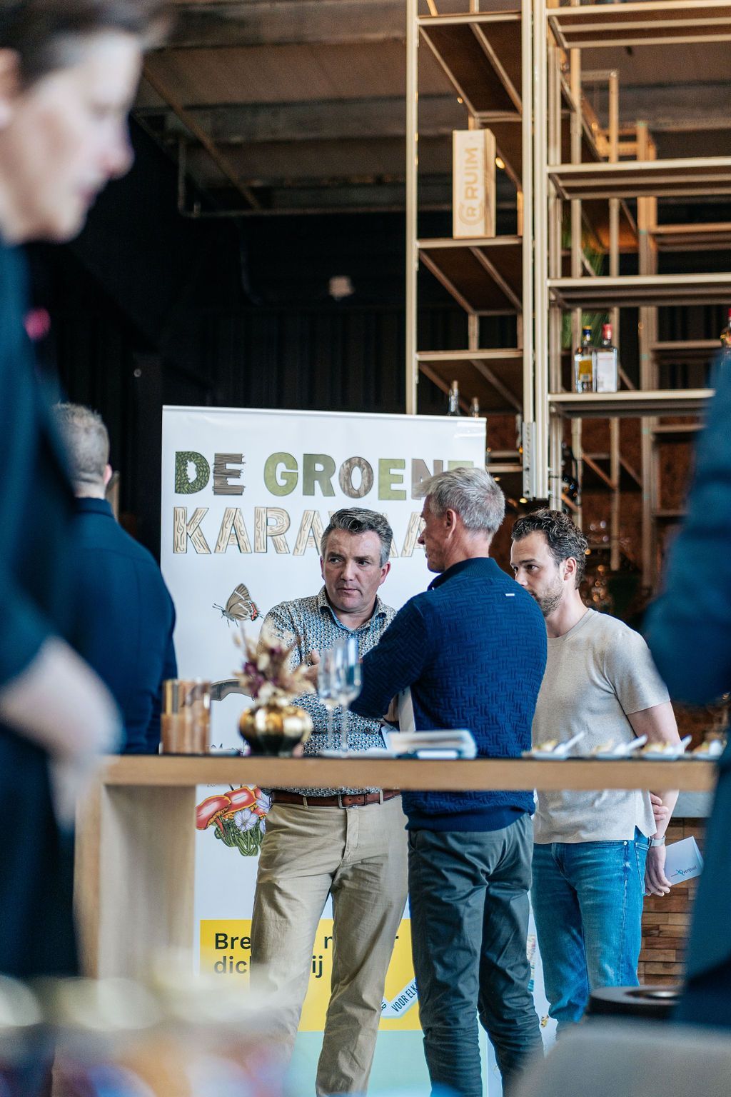 Een groep mensen staat rond een tafel voor een bord met de tekst de groene kara.