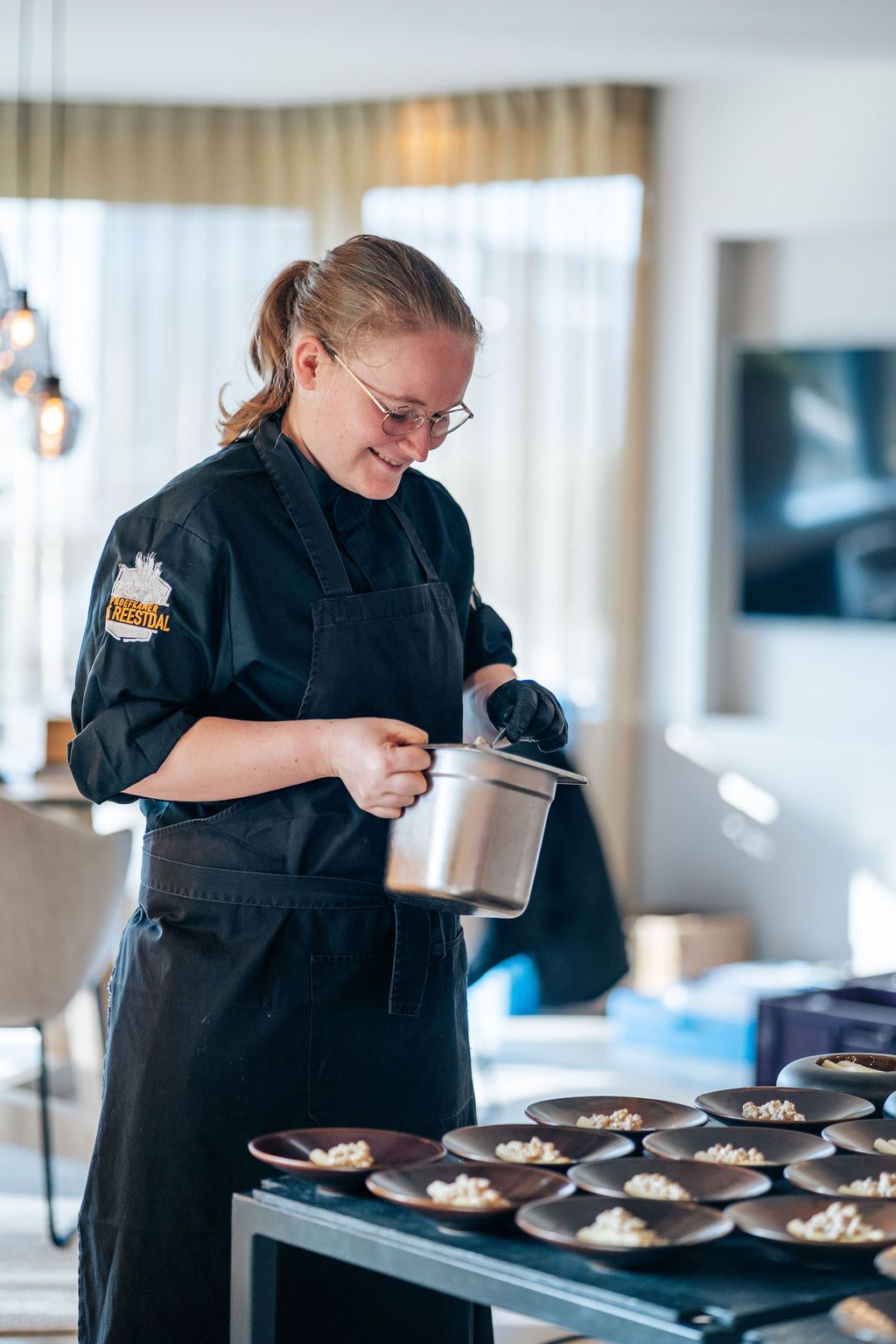 Een vrouw in een zwart schort bereidt eten op een tafel.
